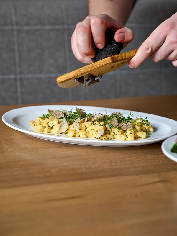 Frische Trüffel werden über cremige Spätzle mit Kräutern auf einem weißen Teller gehobelt